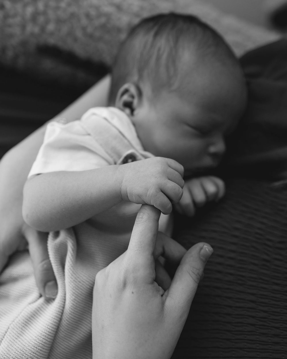 Black and white photo showing a baby's small hand gently holding an adult's finger in tender moment.