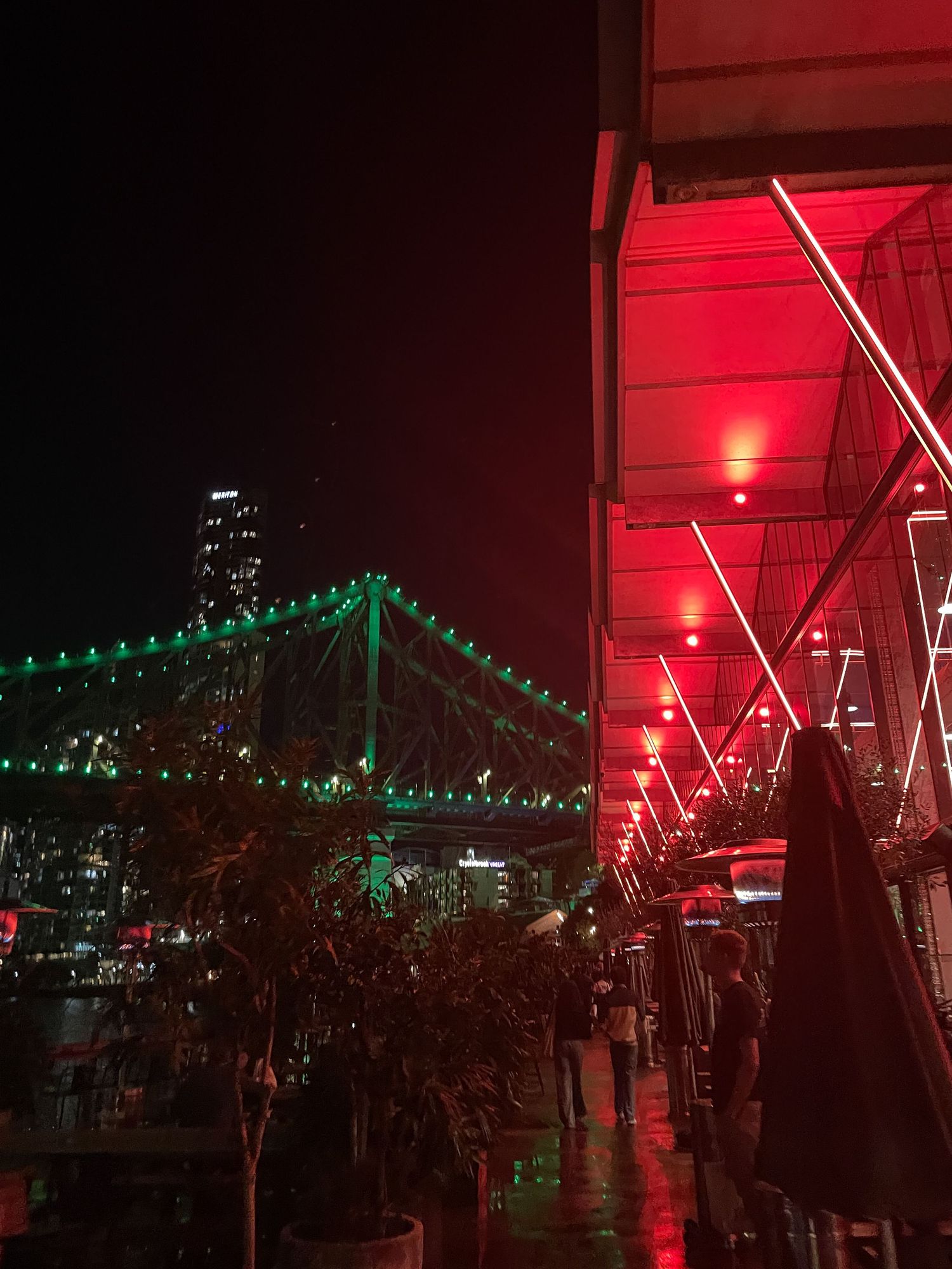 Story Bridge in Brisbane illuminated with green lights at night alongside a walkway with red overhead lighting.