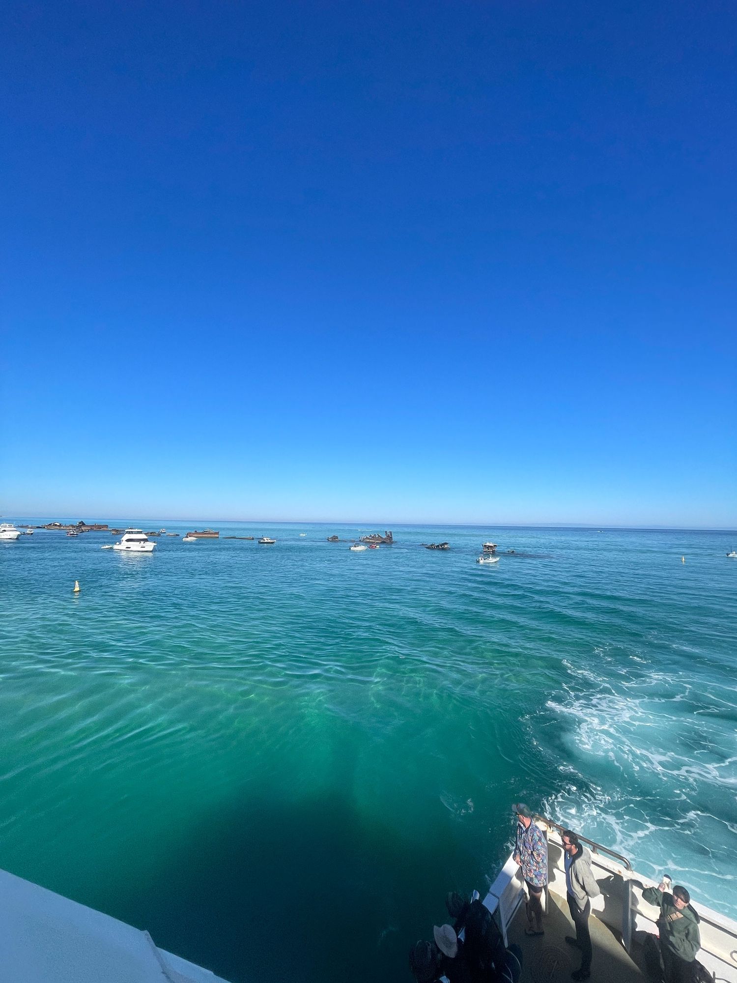 Panoramic view of turquoise ocean waters with boats dotting the horizon under a bright blue sky.