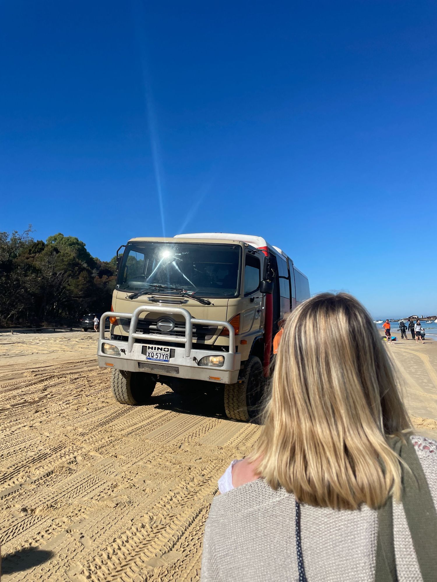 Off-road adventure vehicle parked on sandy beach with clear blue sky on sunny day.