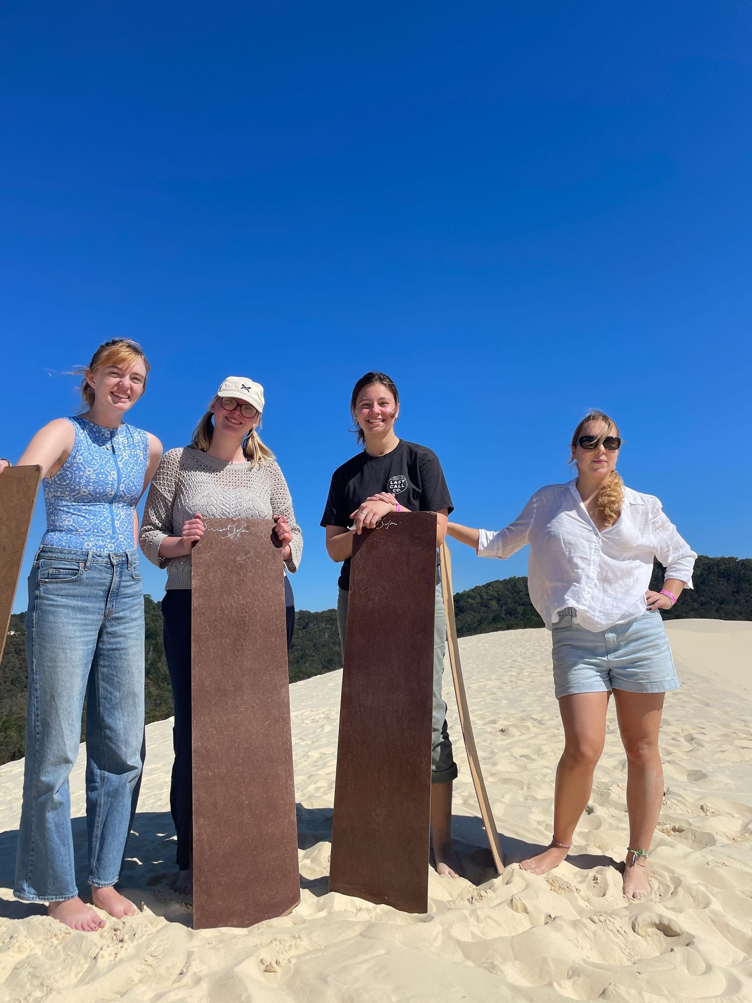 A row of eight people standing behind rustic wooden posts on a sandy beach beneath a bright blue sky.