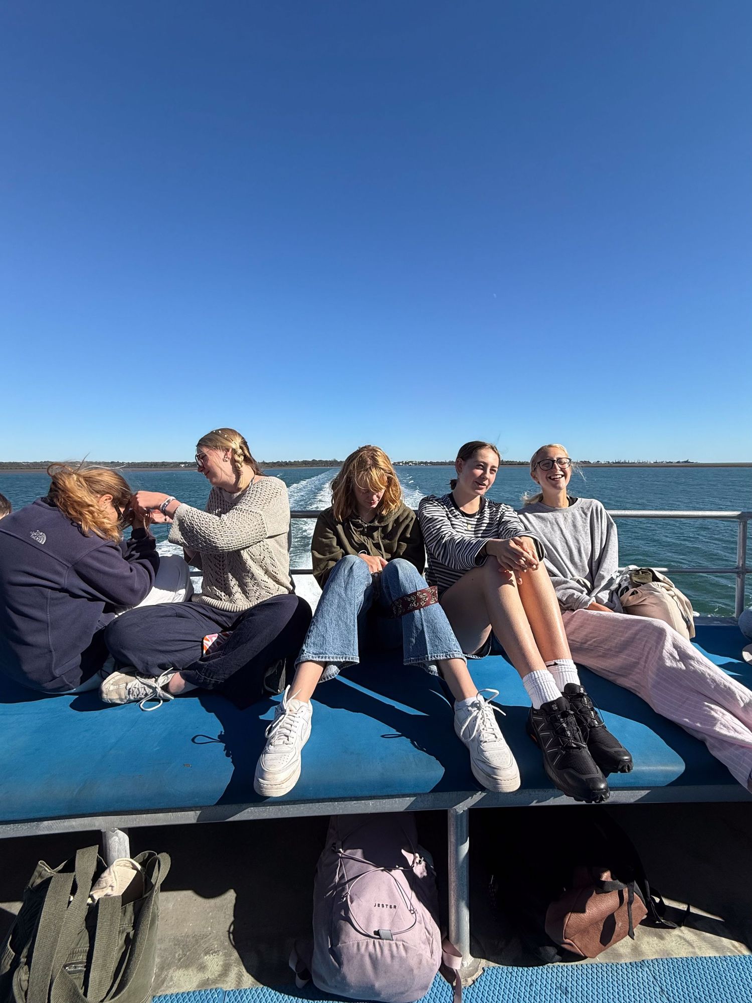 People relaxing and lying down in a row on a blue surface against a clear sunny sky and ocean view.