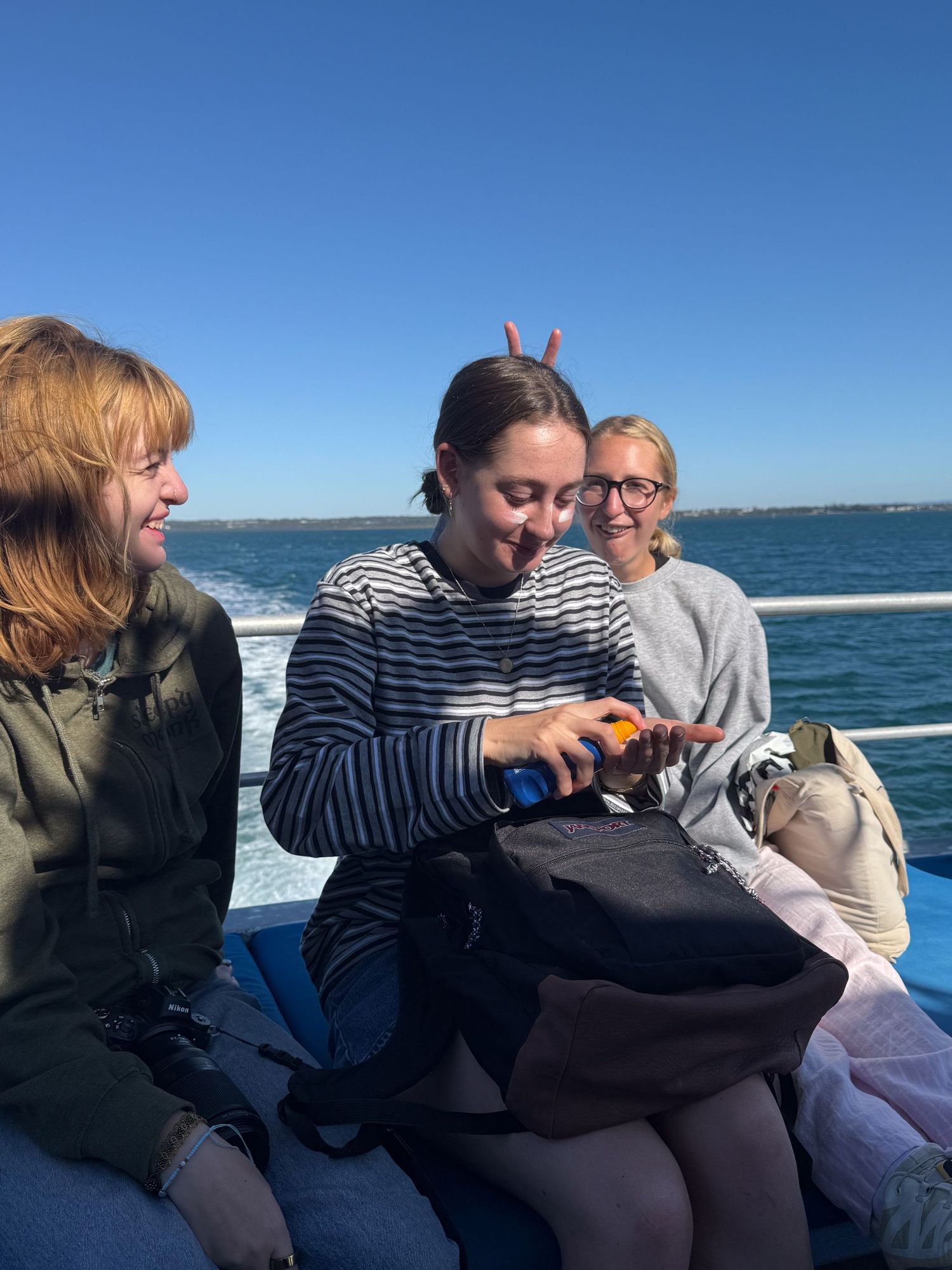 Group seated on a boat deck enjoying snacks and drinks while sailing on sunny waters against blue sky backdrop.