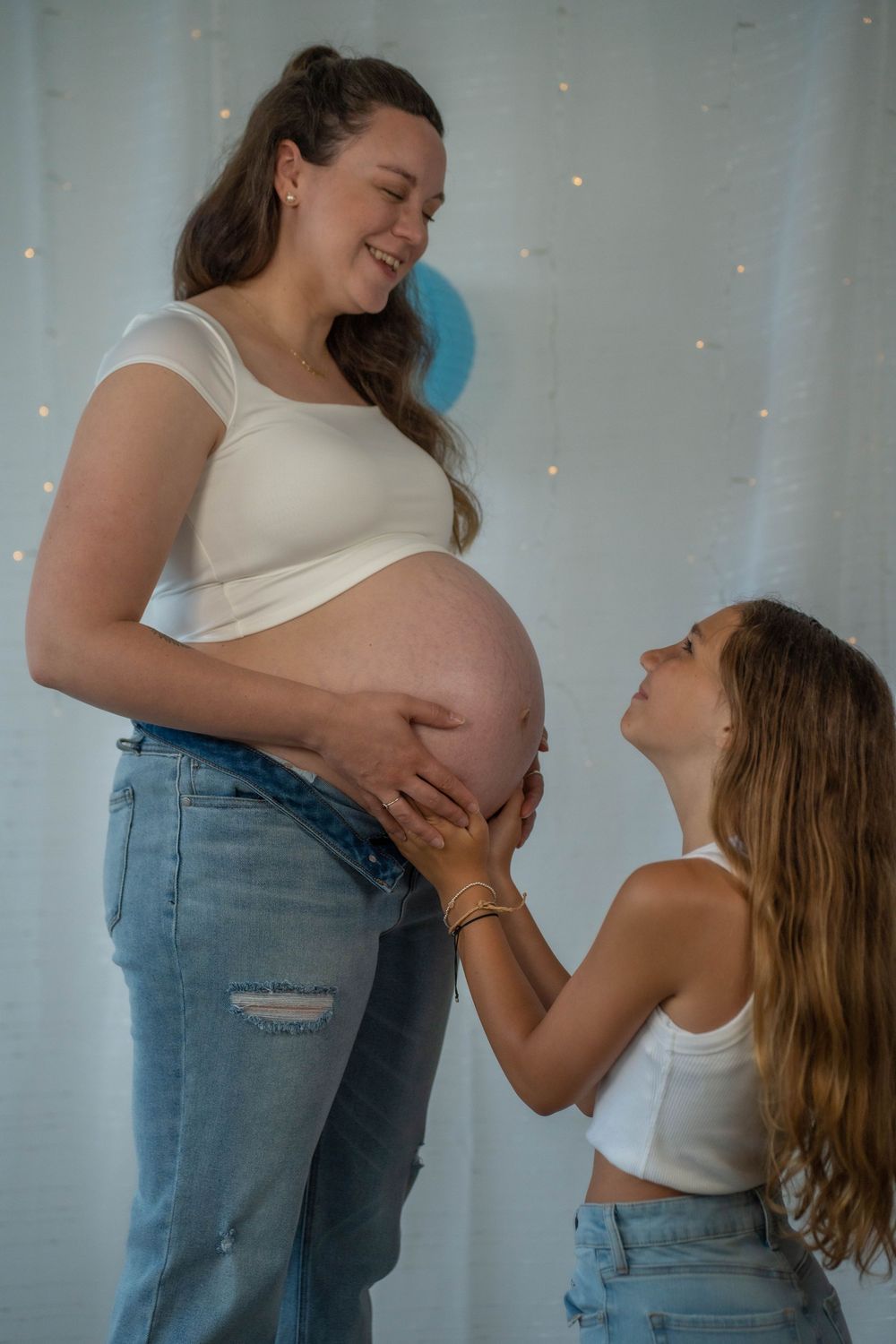 Indoor maternity photoshoot with white backdrop and gentle lighting.