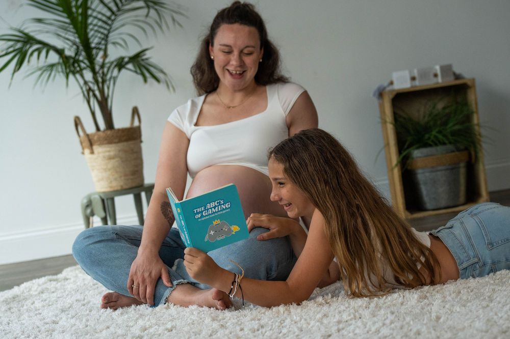 Relaxed indoor maternity photoshoot featuring people reading and lounging together.