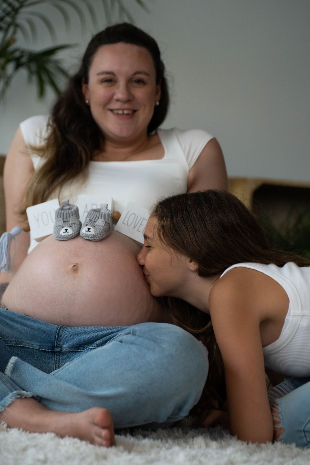 Two people in casual attire sharing intimate moments during a maternity photoshoot.
