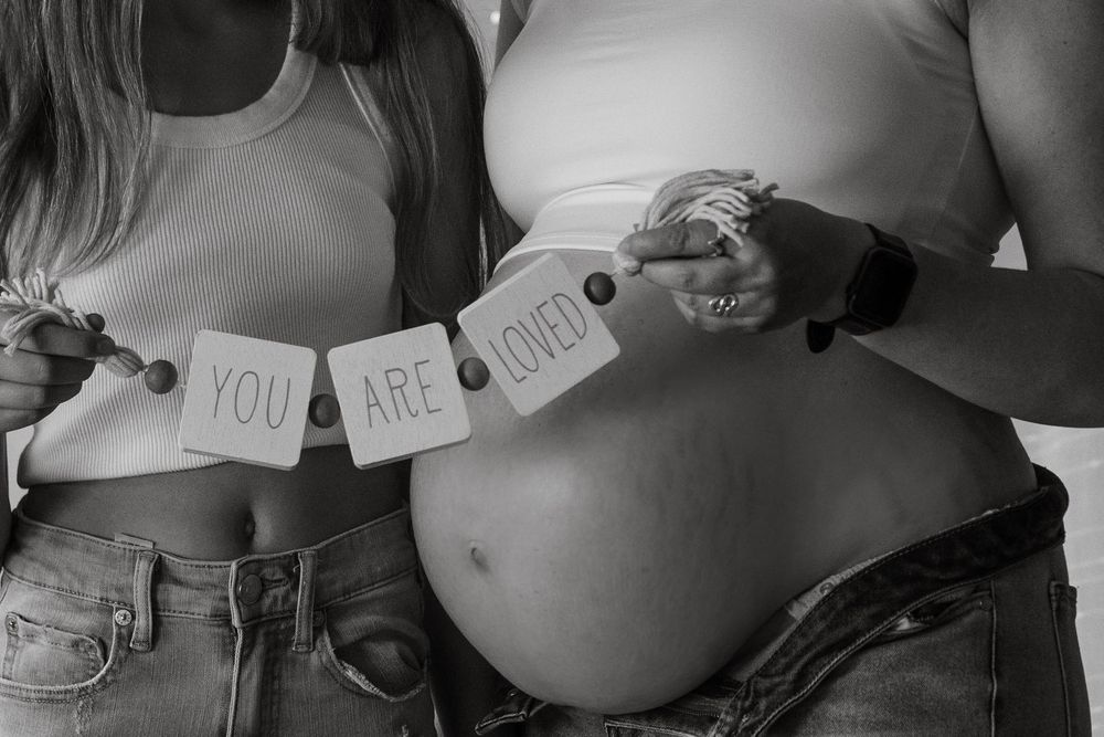 Series of black and white photos showing a pregnancy announcement with handwritten signs on bellies.
