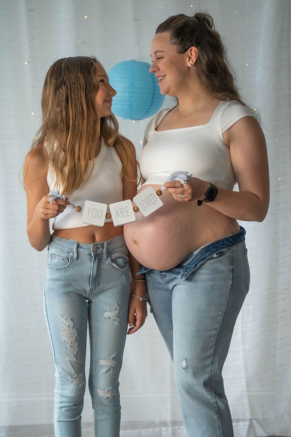 Two people in white tops and jeans posing together during a casual indoor photoshoot.