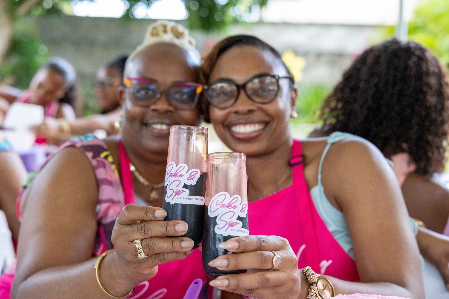 A mother and daughter, both wearing pink aprons, smiling together at the Mother's Day Cake & Sip by Sweet Divine event in St. Kitts.