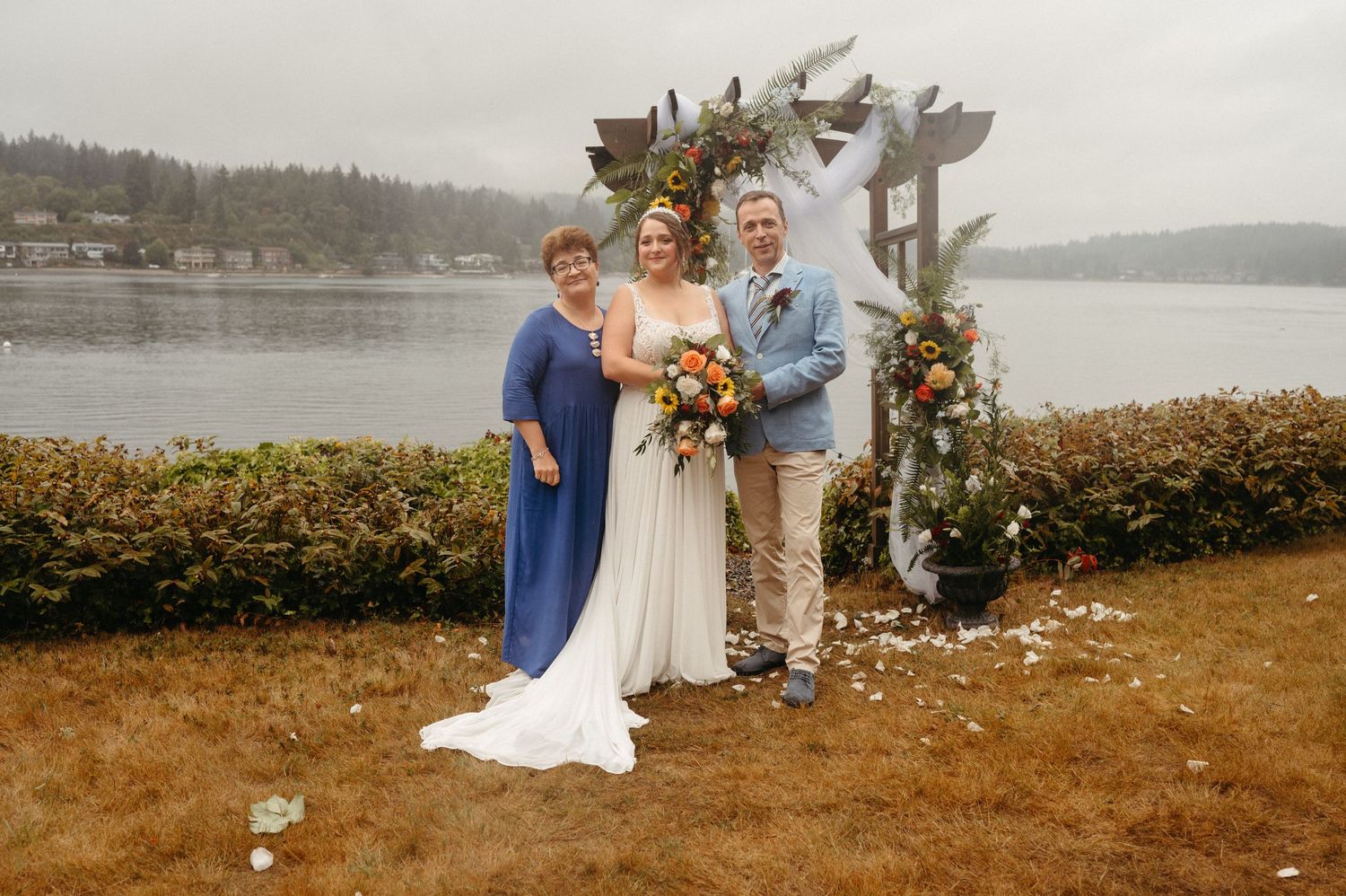 Outdoor wedding ceremony under a floral arch overlooking a serene lake with mountains in the background.