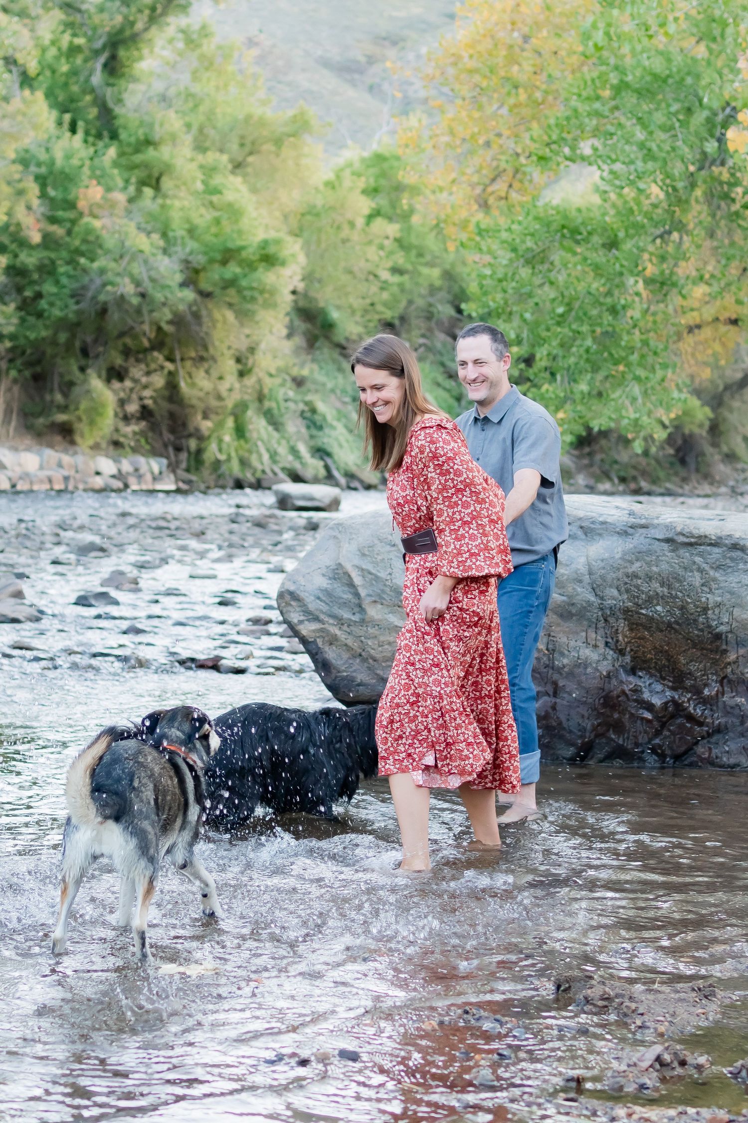 Couple plays with their dog in mountain stream during engagement photo session.