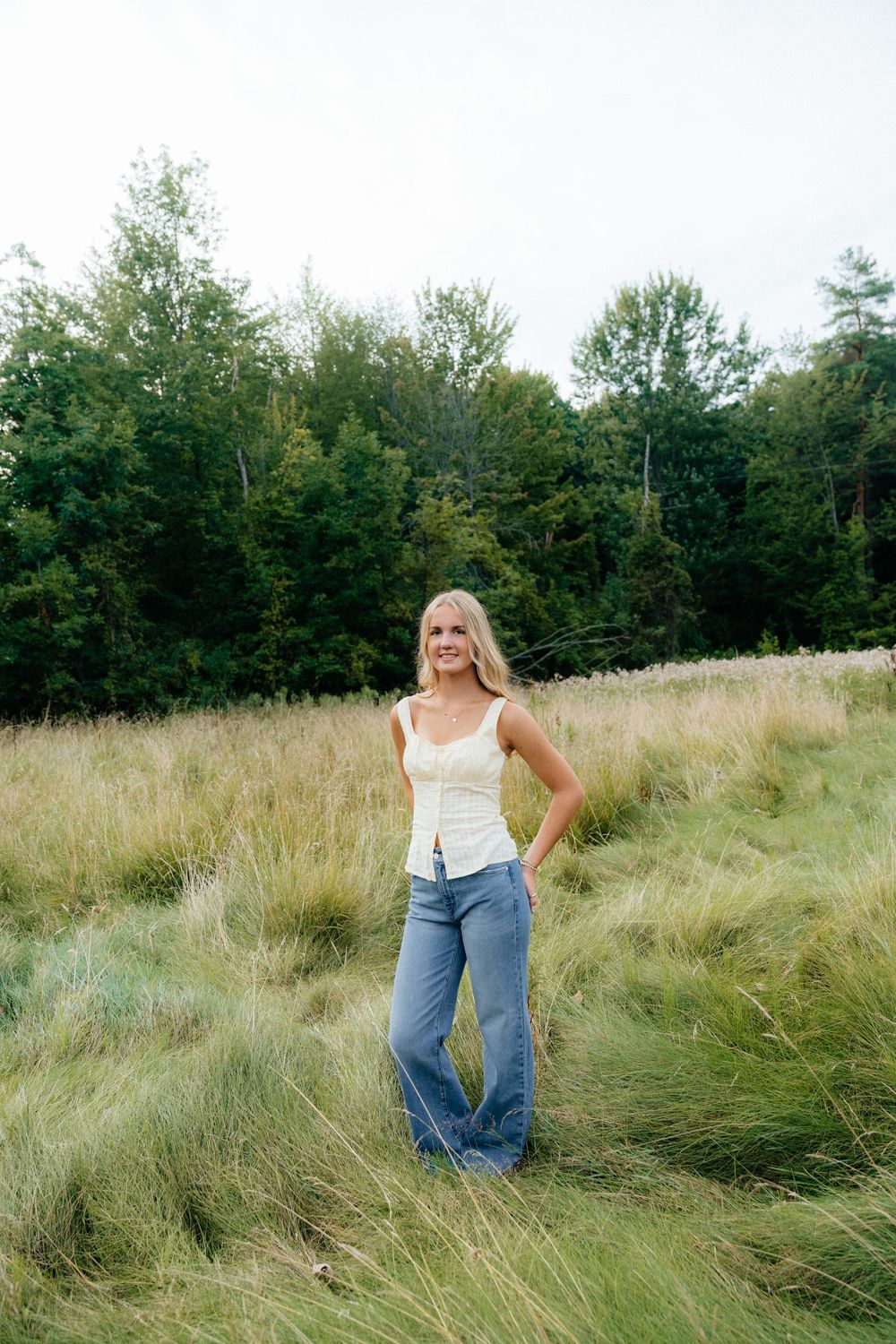 Candid poses in tall grass meadow with trees in background during golden hour.