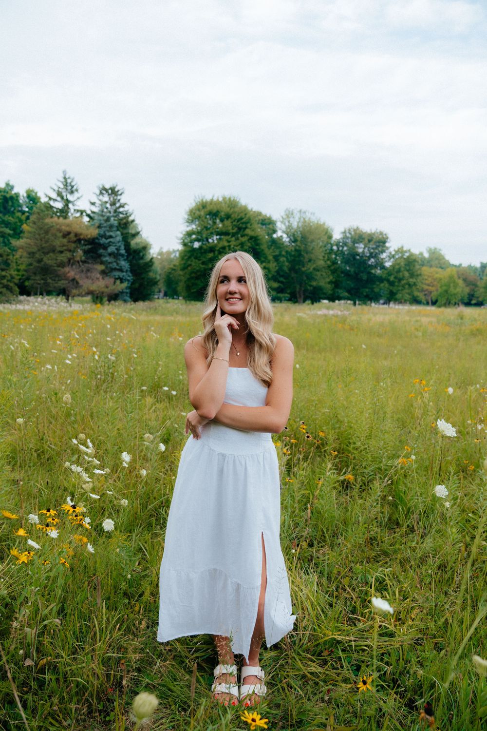 A white sundress outfit photographed in a wildflower meadow with tall grass and yellow flowers.