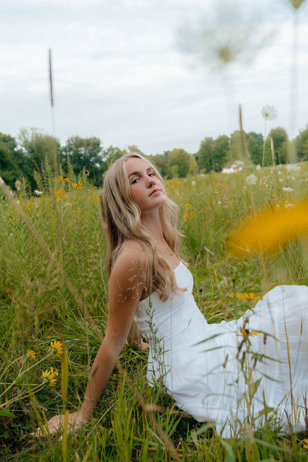 A dreamy summer portrait in a white dress amid yellow wildflowers and tall grass.