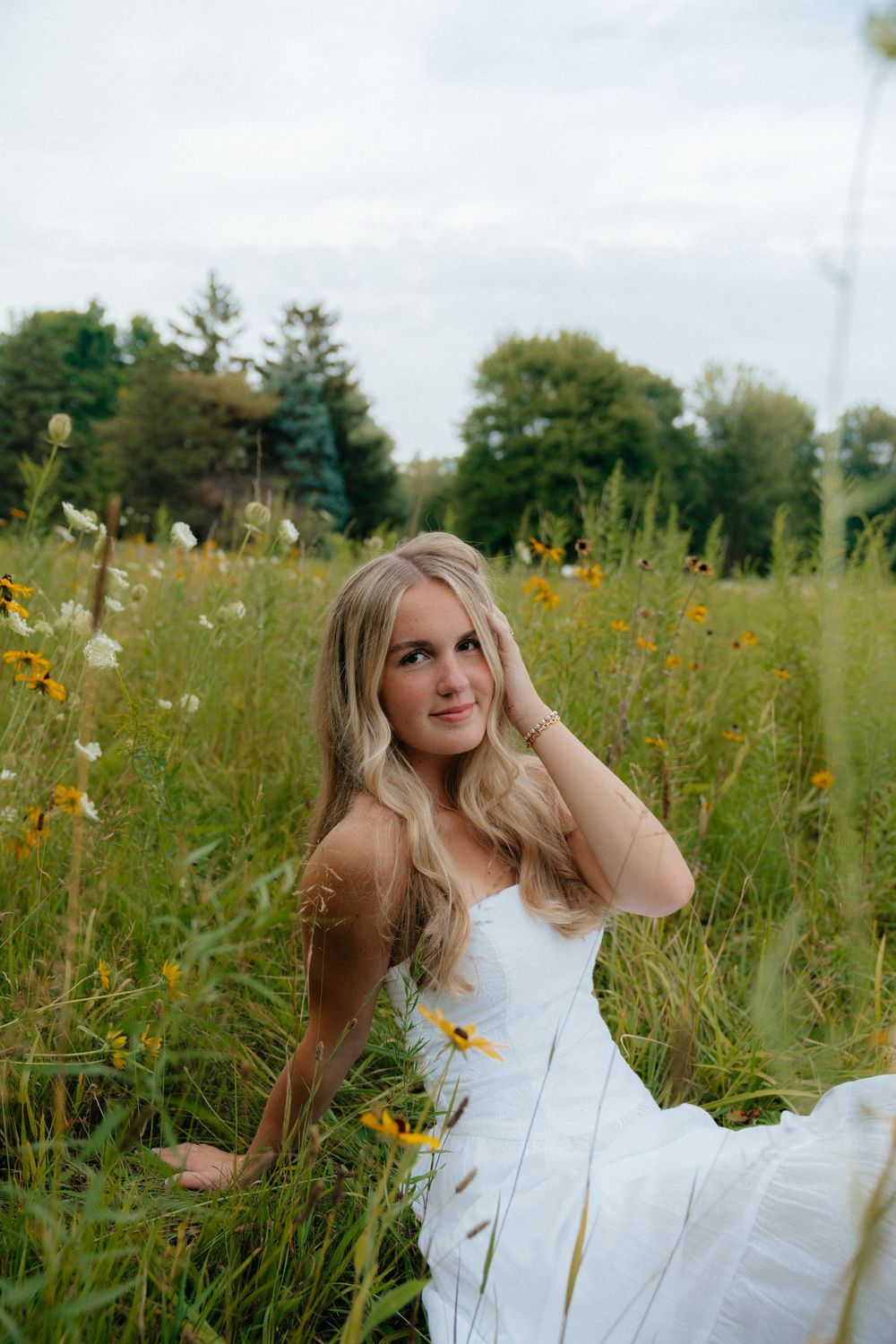 Summer portrait in a white dress surrounded by yellow wildflowers in a natural meadow setting.