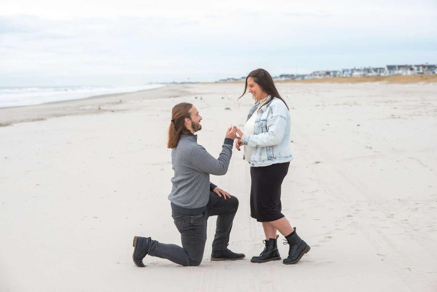 A proposal scene on a beach with one person kneeling in the sand.