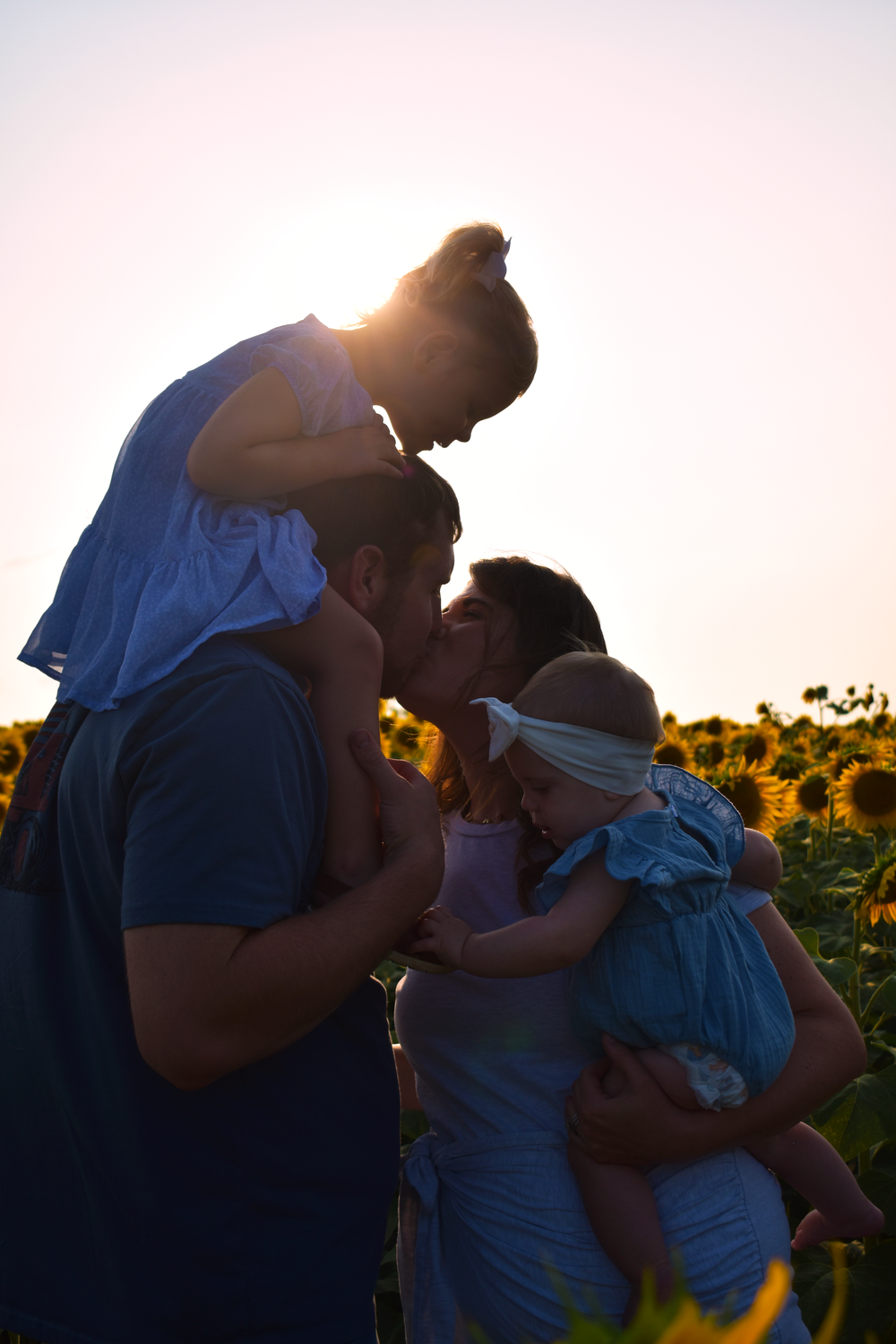 Family sharing tender moment in sunflower field at sunset.