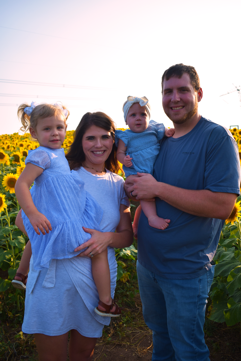 Family poses for portrait in sunflower field during golden hour.
