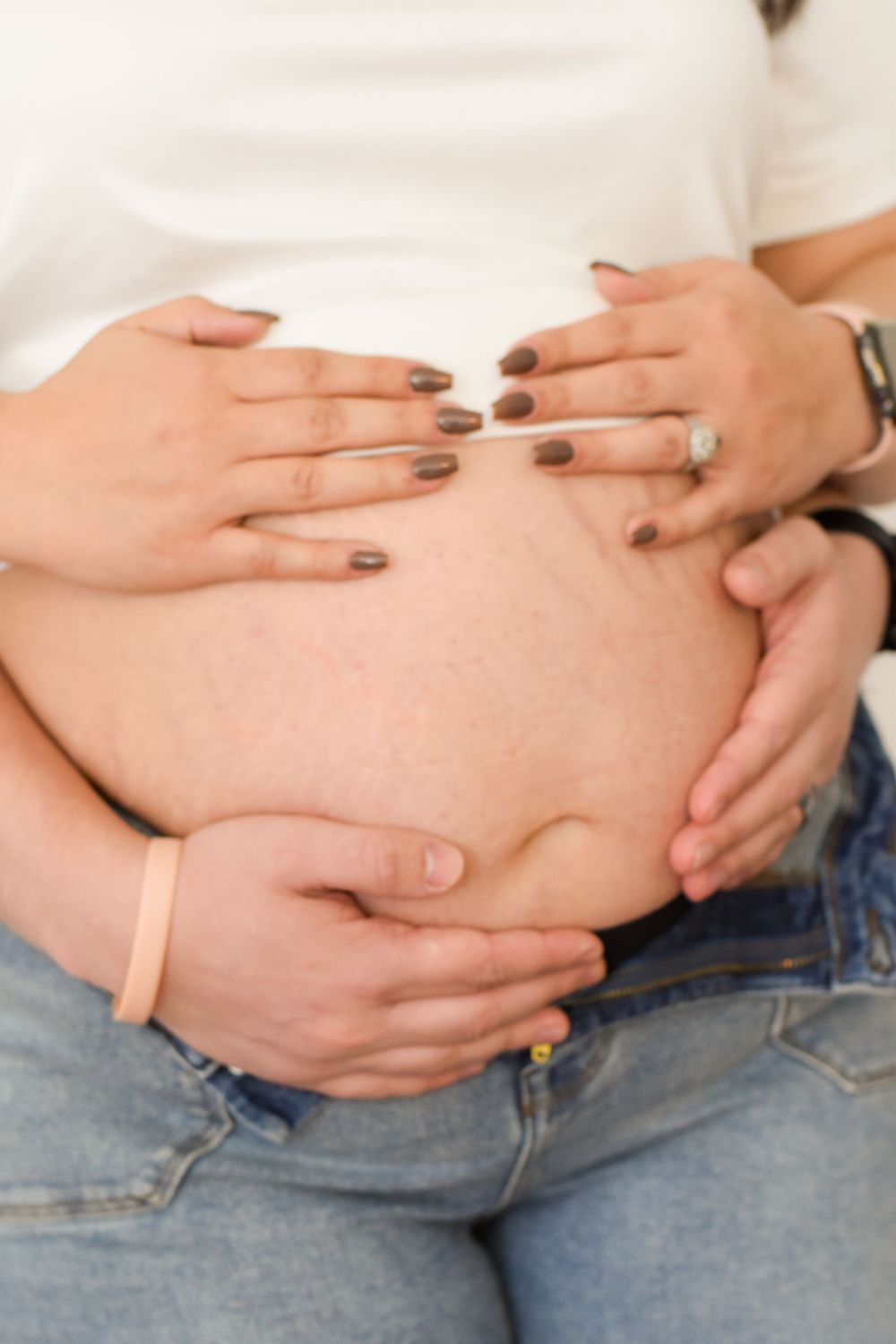 Close-up view of hands cradling a pregnant belly wearing blue jeans and white top.