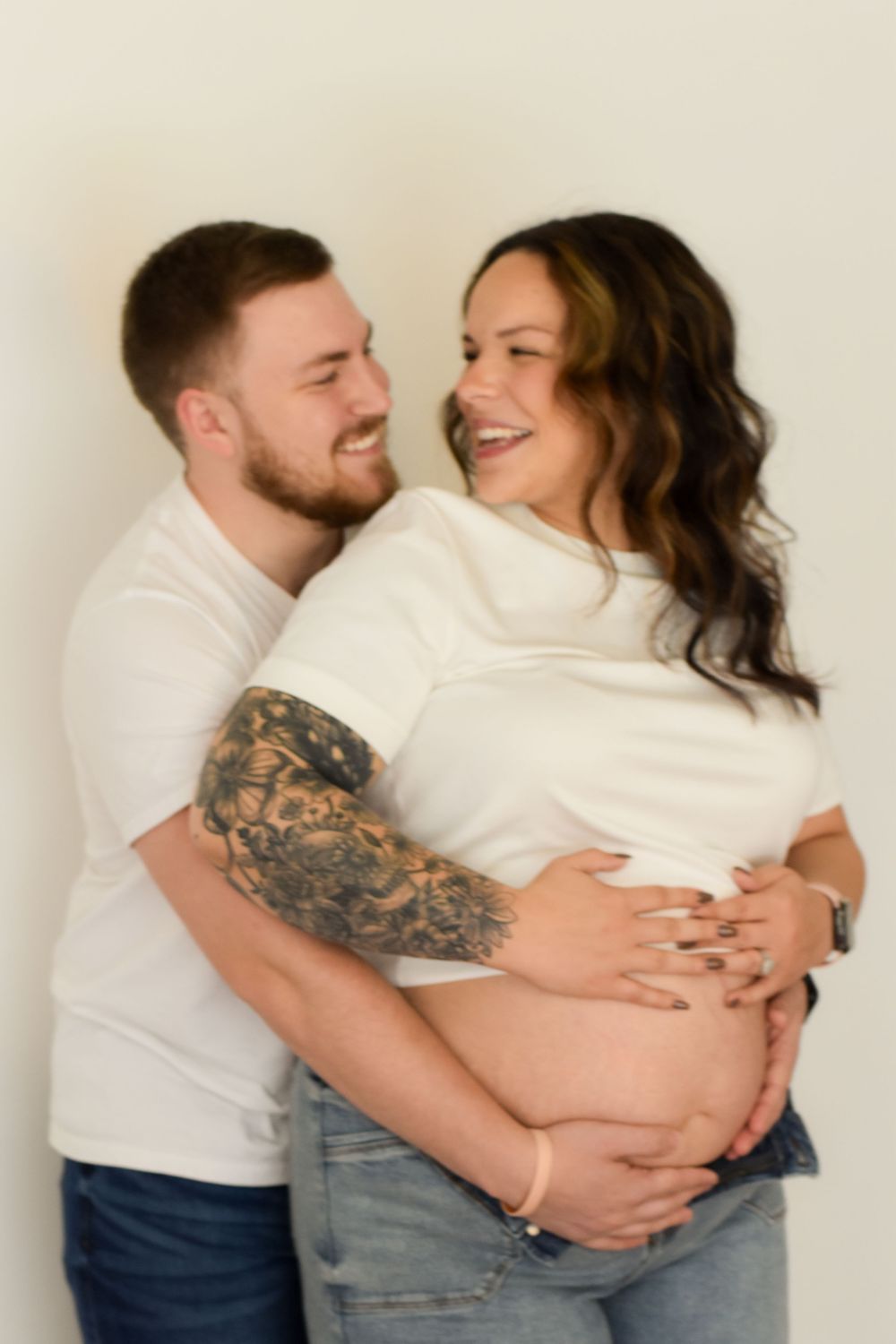 A couple shares an intimate moment as they pose together for a pregnancy photoshoot in white and denim outfits.
