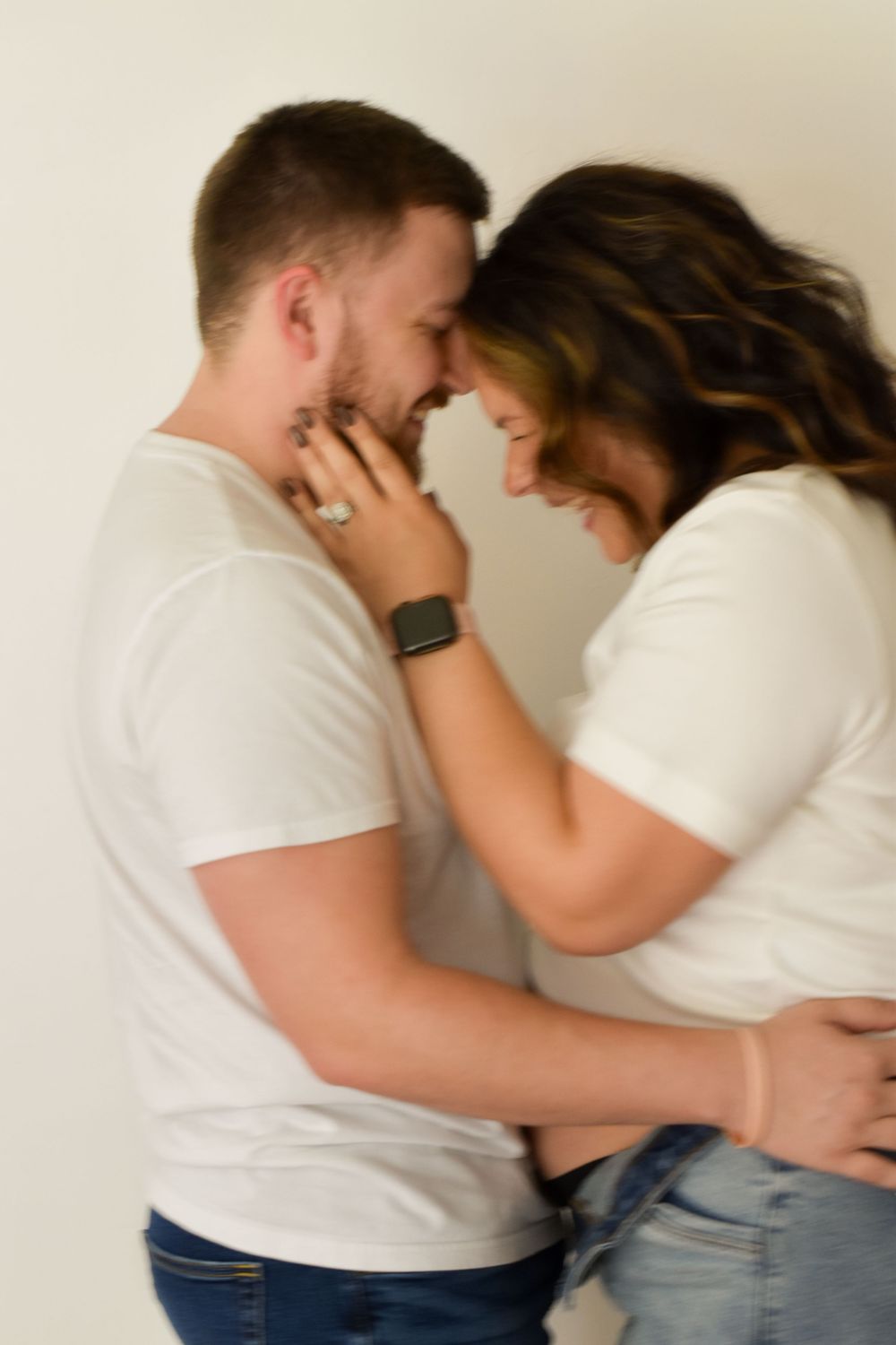 An intimate candid moment between a couple in matching white shirts during a pregnancy photoshoot.