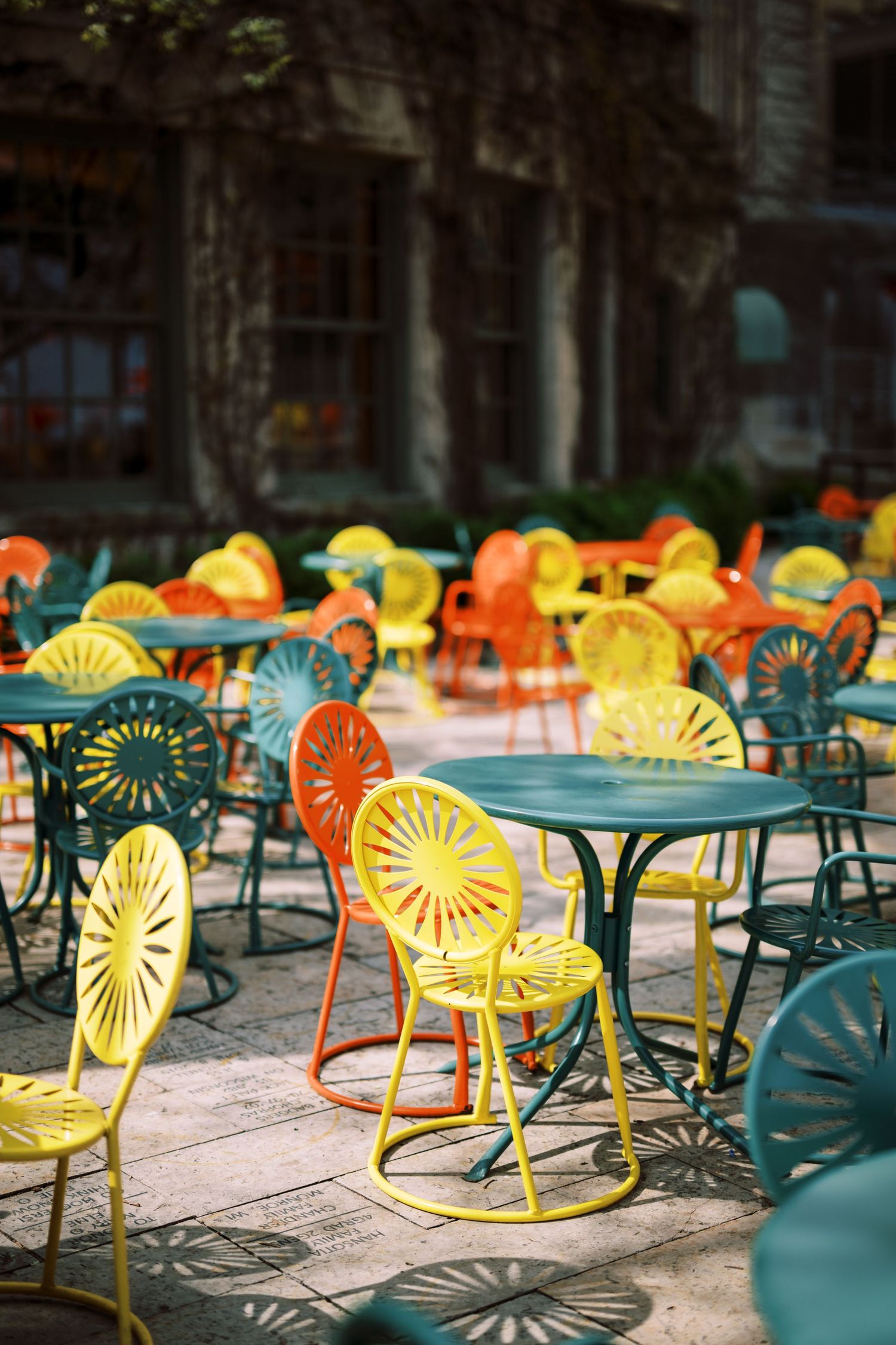 Colorful retro metal chairs and tables arranged outdoors with vibrant yellow, orange and turquoise sunburst designs.