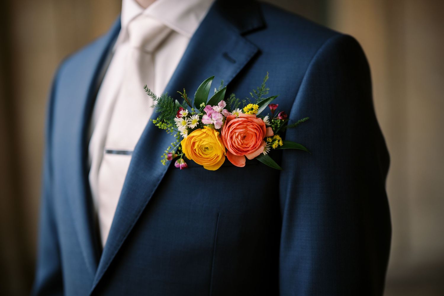 Close-up of orange and yellow floral boutonniere on navy blue suit jacket lapel.