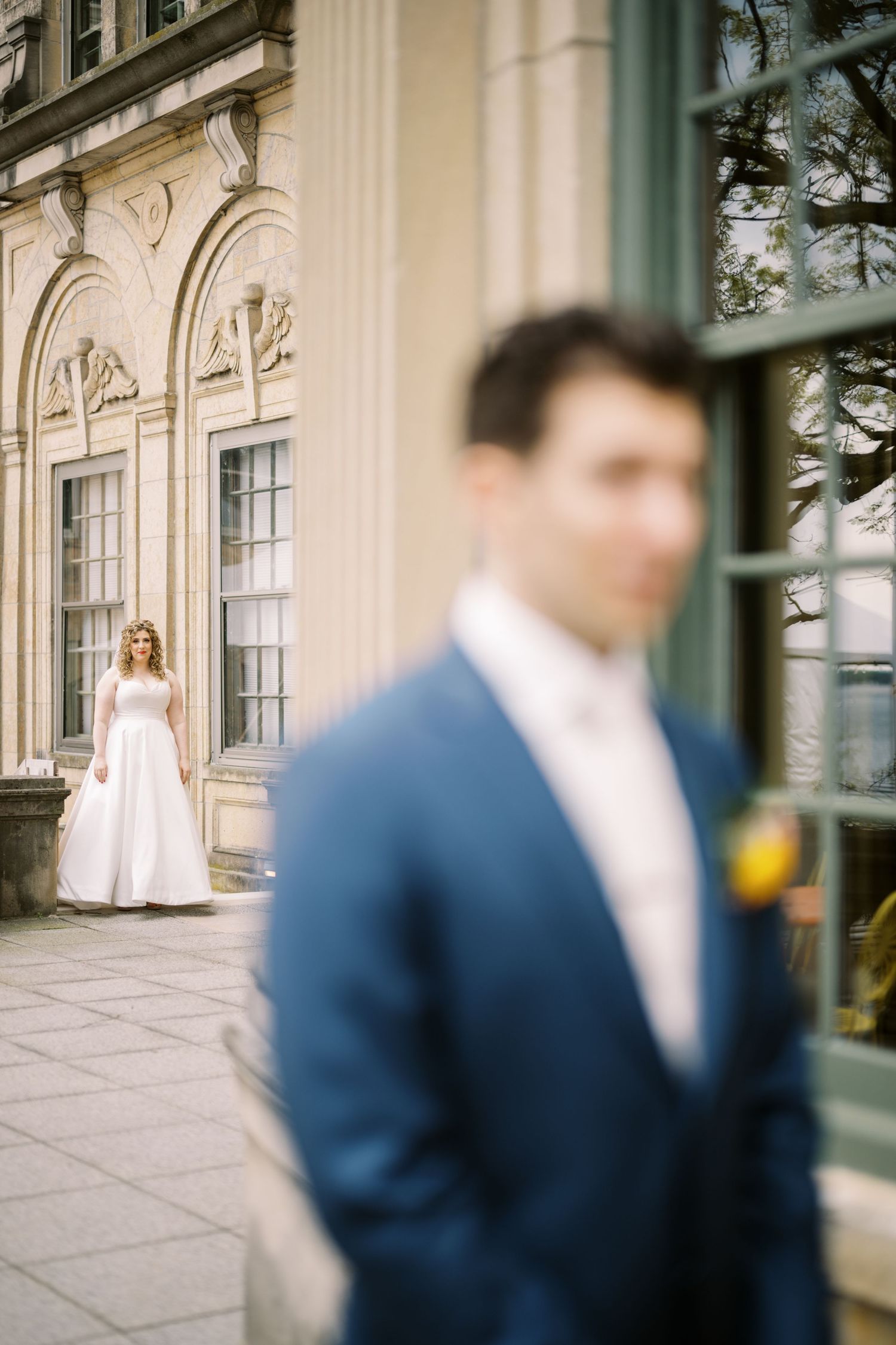 Wedding couple posing separately outside historic building with classical architecture.