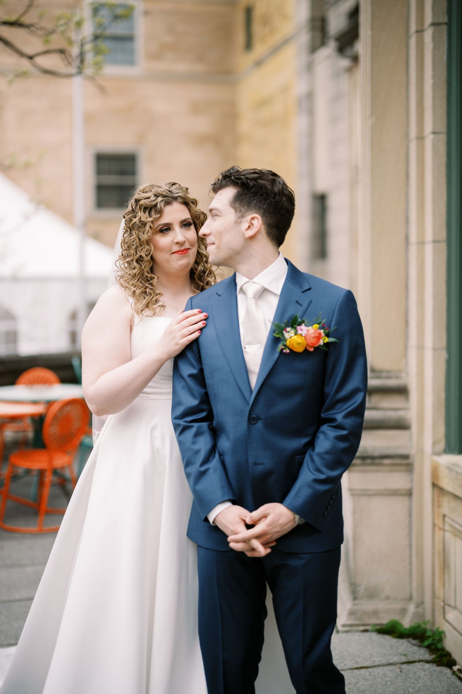 Wedding couple in elegant attire sharing an intimate moment against stone building backdrop.