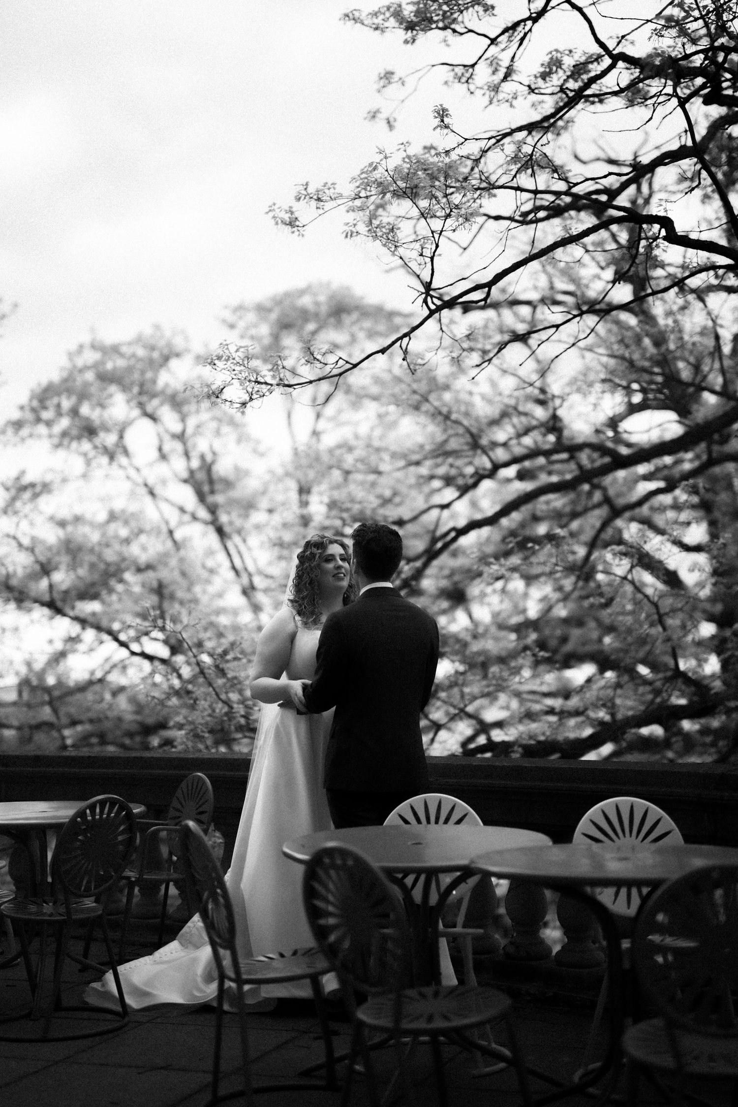Black and white silhouette of couple overlooking garden with vintage metal chairs in foreground.