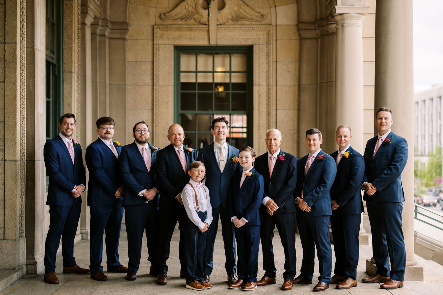 Group in navy suits posed formally outside classical stone building.