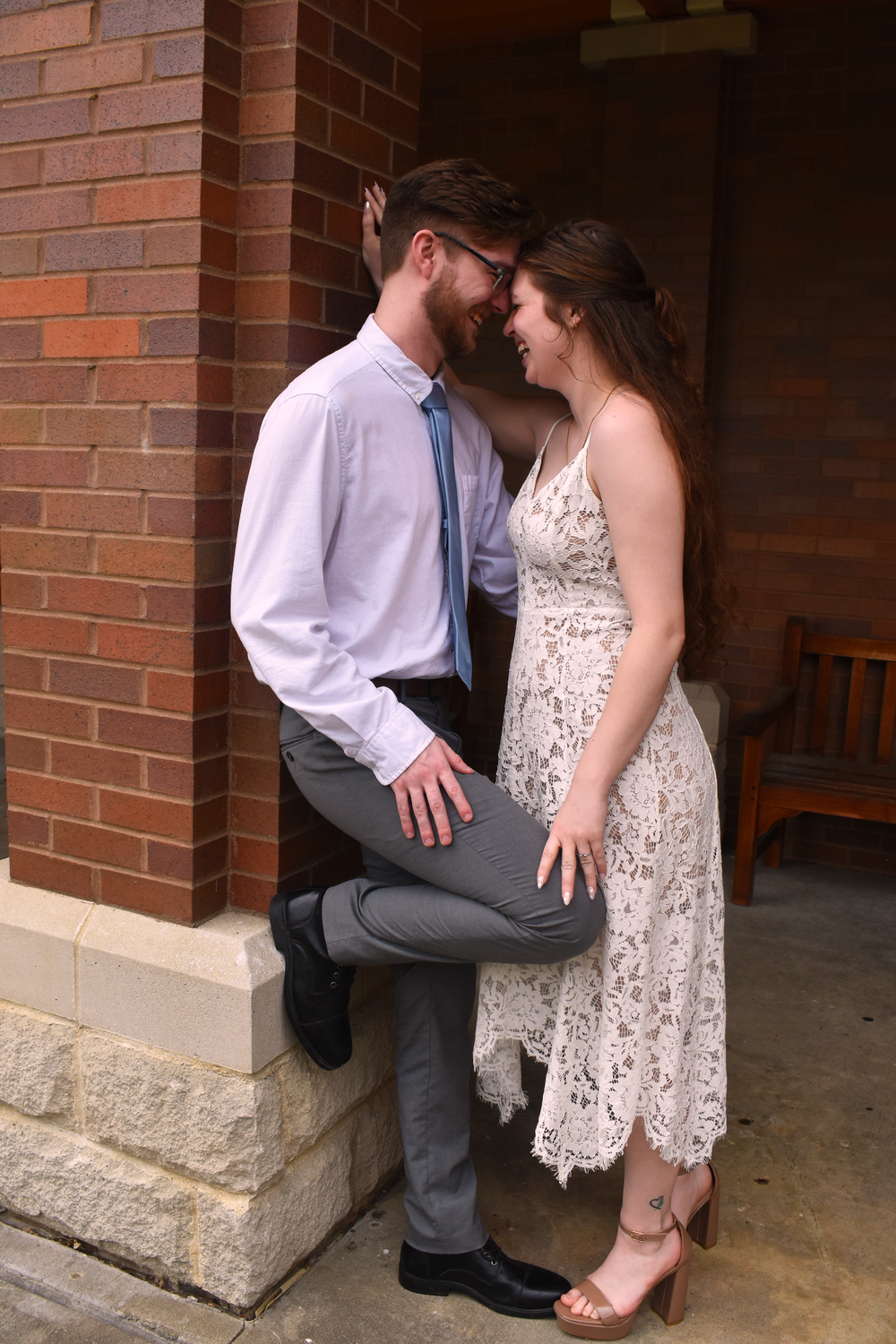 A romantic moment between a couple in formal attire against a brick wall.