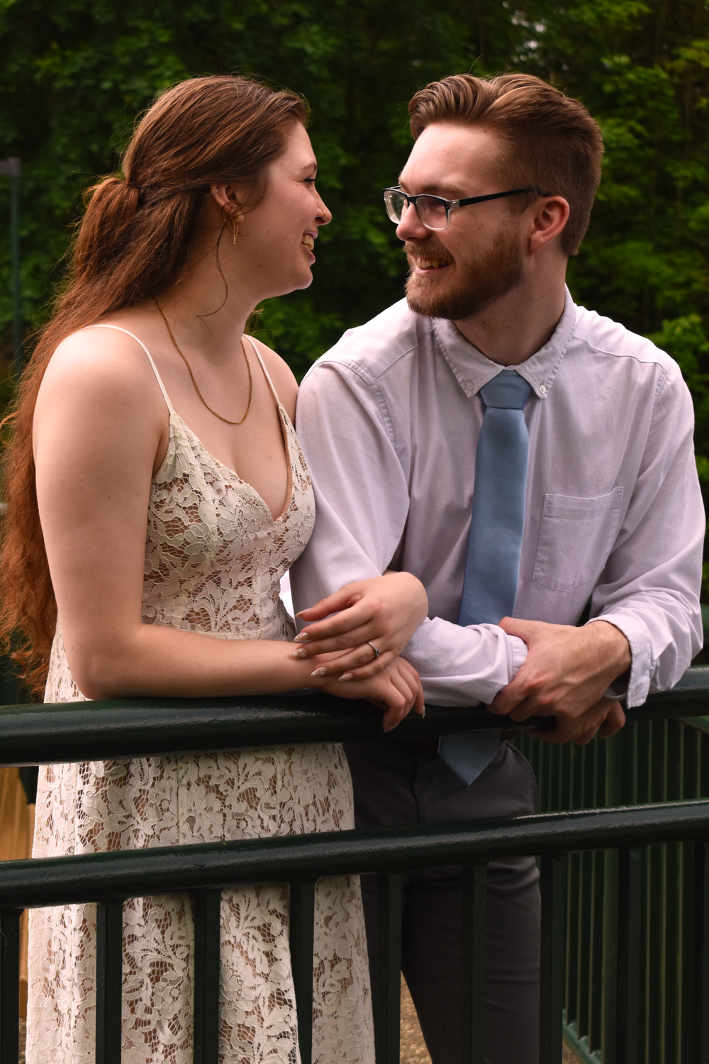 A couple shares a laugh while leaning against a railing outdoors.
