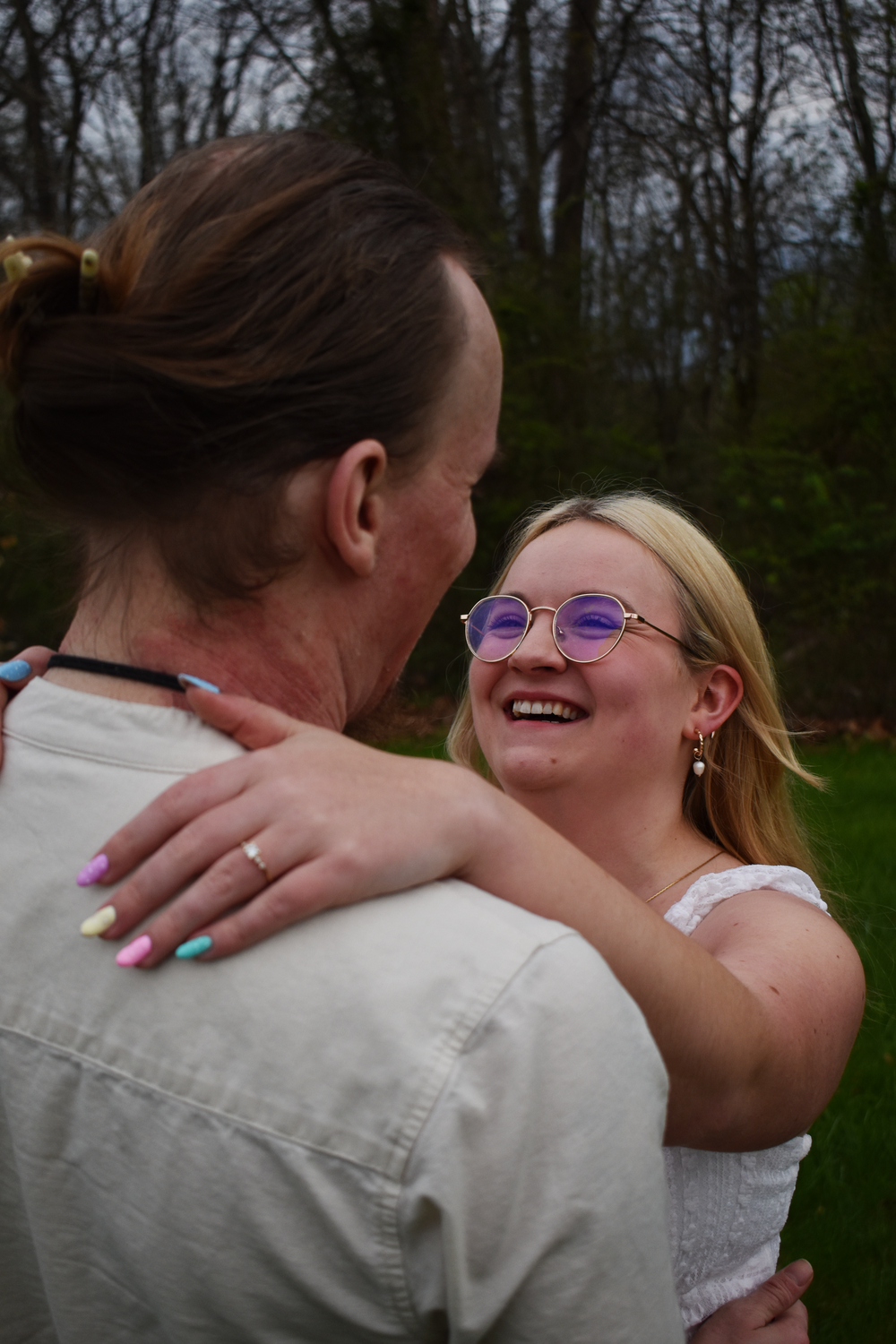 A romantic outdoor moment of a couple embracing and smiling together in a wooded setting.