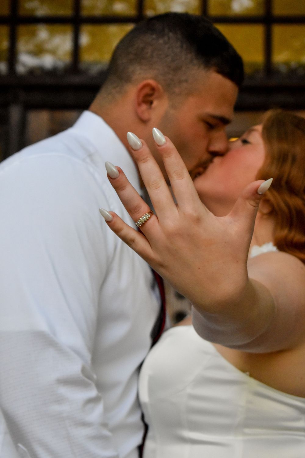 A romantic wedding kiss with the bride's engagement ring in focus as she holds her hand up during their intimate moment.