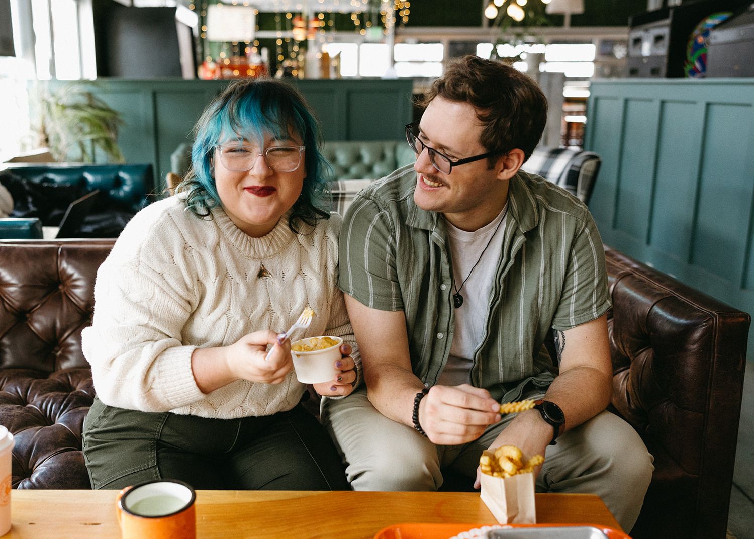 Two people share coffee and conversation while sitting at a wooden table in a cozy cafe setting.
