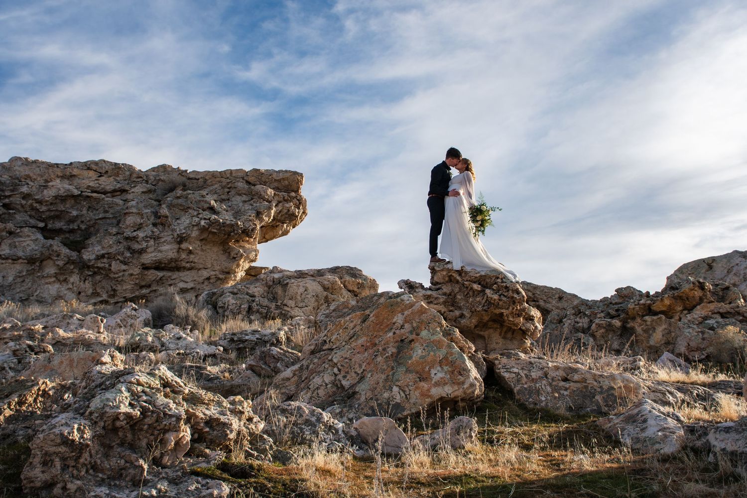 Couple kisses in a cinematic photo in front of Utah mountain landscape.