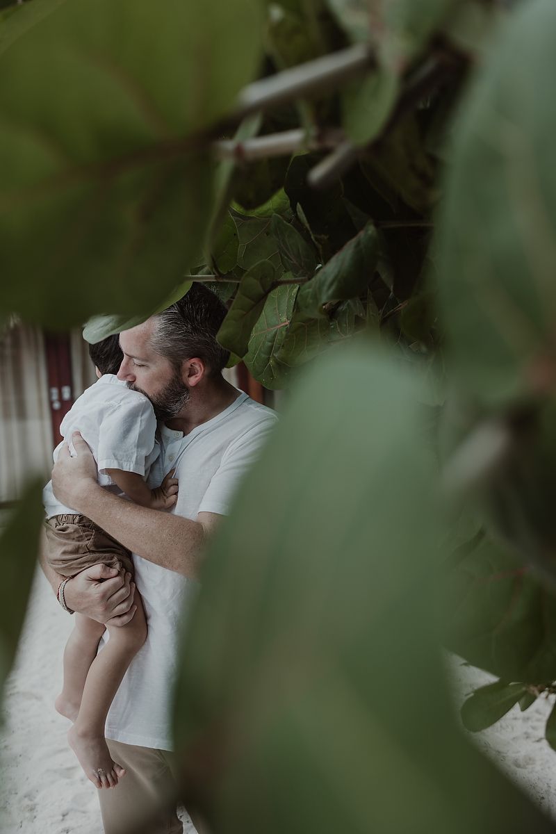 Father playing with son among tropical greenery during family vacation photos in Tulum.
