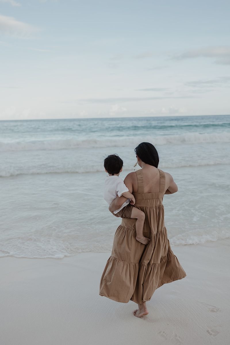 Mother walking by the Caribbean Sea with child during family beach photoshoot in Tulum.