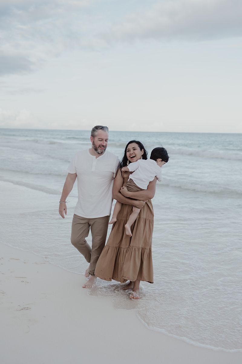Parents embracing with child on the shoreline at La Zebra Hotel, Riviera Maya family portraits.