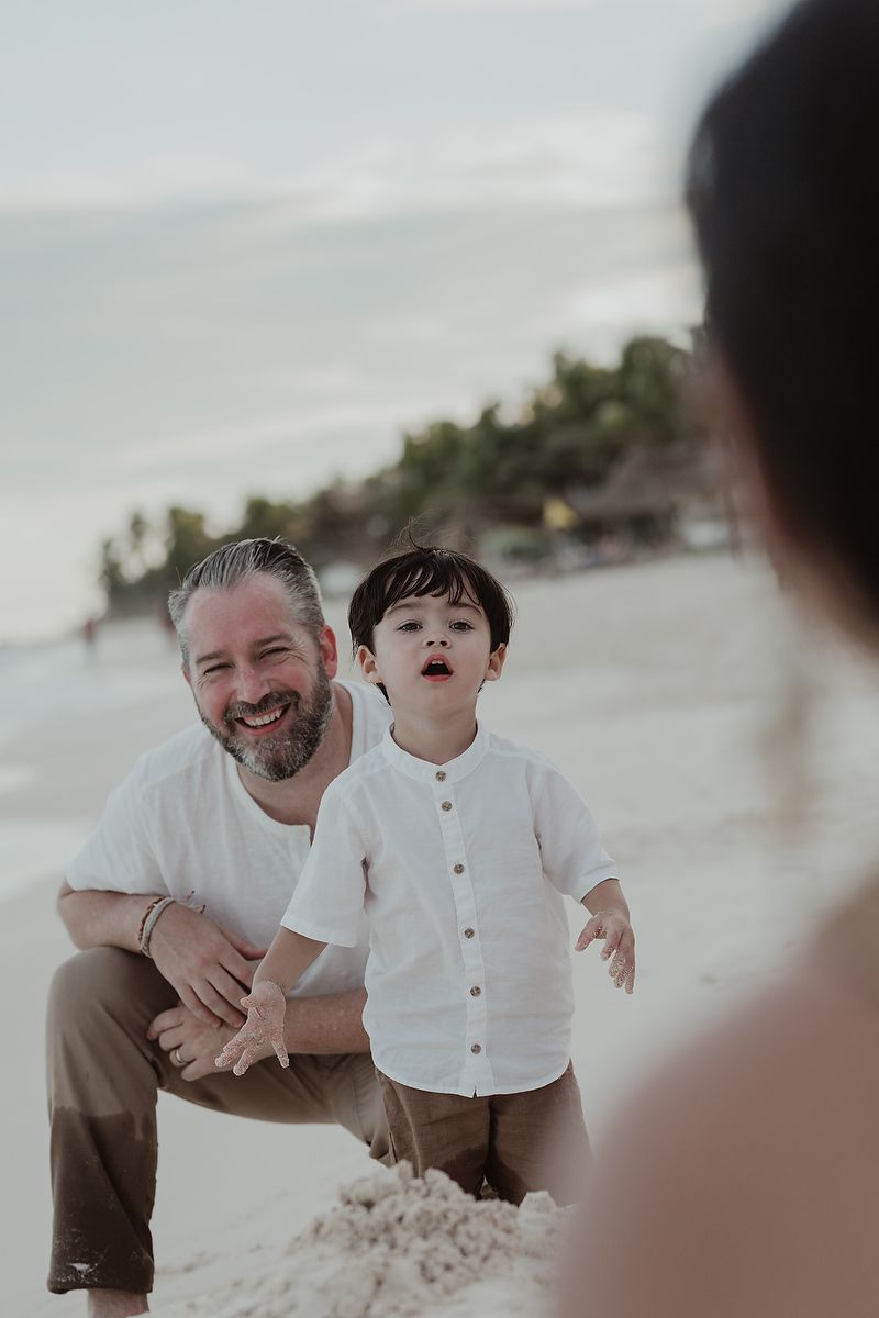 Father kneeling and smiling with son during playful family vacation photoshoot in Tulum.