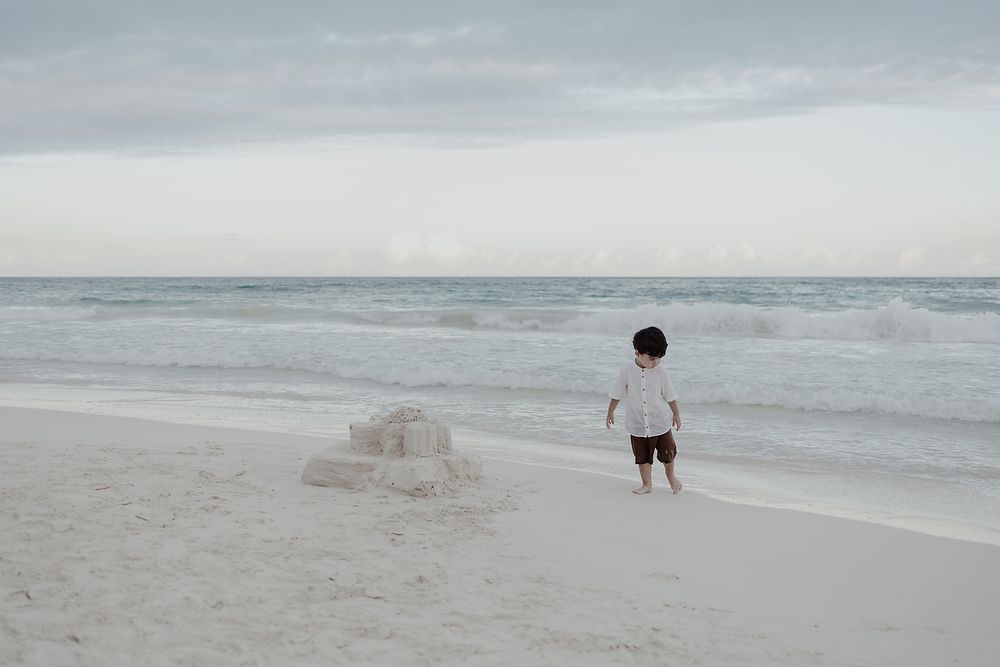 Child playing by the sea with sandcastle during Tulum family beach photoshoot.