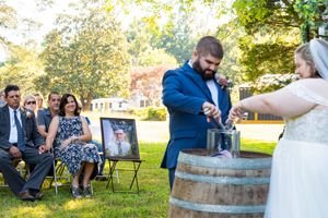 Wedding party poses with rustic wine barrels in an outdoor garden setting during golden hour.