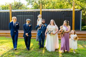 Wedding group stands in front of black fence panels in a sunny outdoor garden setting.