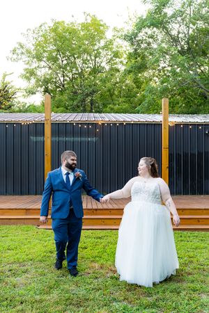 A bride and groom share a playful moment in a garden setting with a wooden fence backdrop.