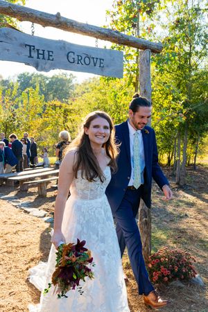 A wedding ceremony takes place at The Grove venue with a rustic wooden entrance sign and autumn foliage in the background.