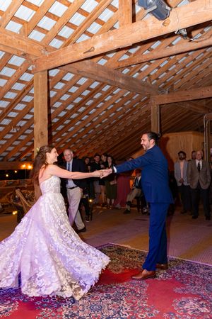 A couple performs a romantic dance move on a red carpet in a rustic barn venue with latticed wooden ceiling.
