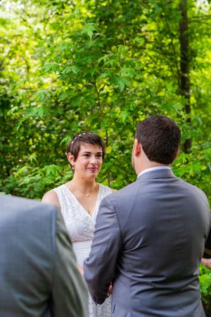 Bride and groom exchange vows outdoors surrounded by lush green trees during an intimate wedding ceremony.