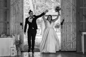 A celebratory wedding entrance with dancing and raised arms in a rustic barn setting.