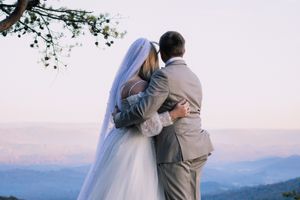 Wedding couple embraces while overlooking mountain vista in soft light.